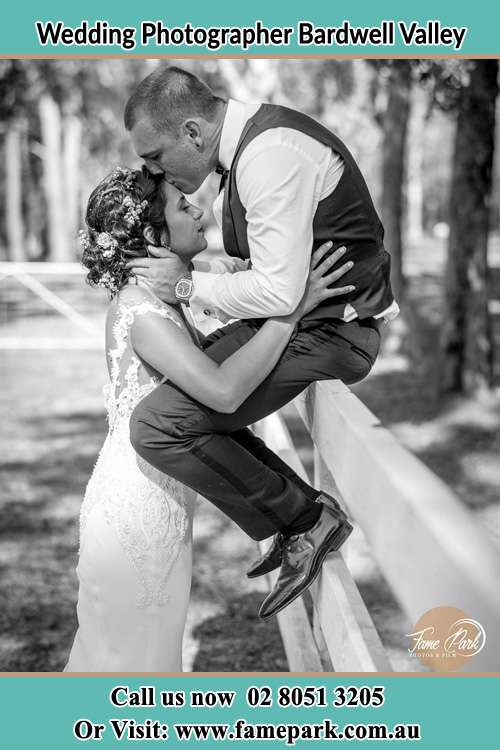 Photo of the Groom sitting on the fence while kissing the Bride on the forehead Bardwell Valley NSW 2207