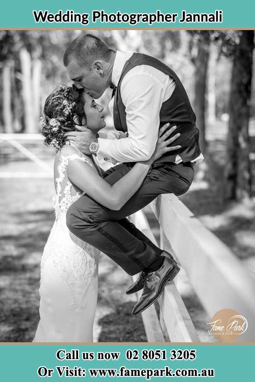 Photo of the Groom sitting on the fence while kissing the Bride on the forehead Jannali NSW 2226